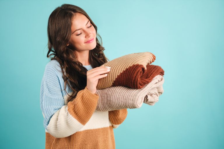Beautiful cute girl dreamily holding knitted sweaters in hands o